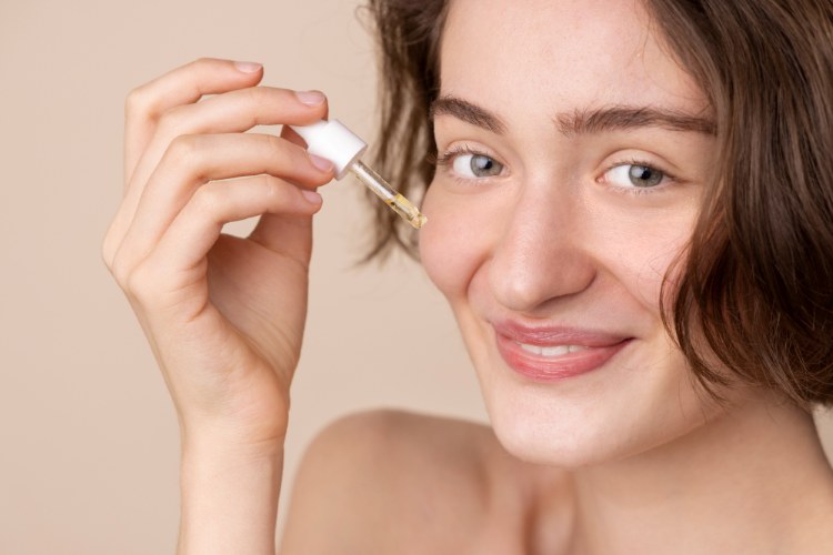 A woman happily applying a retinoid serum on her face