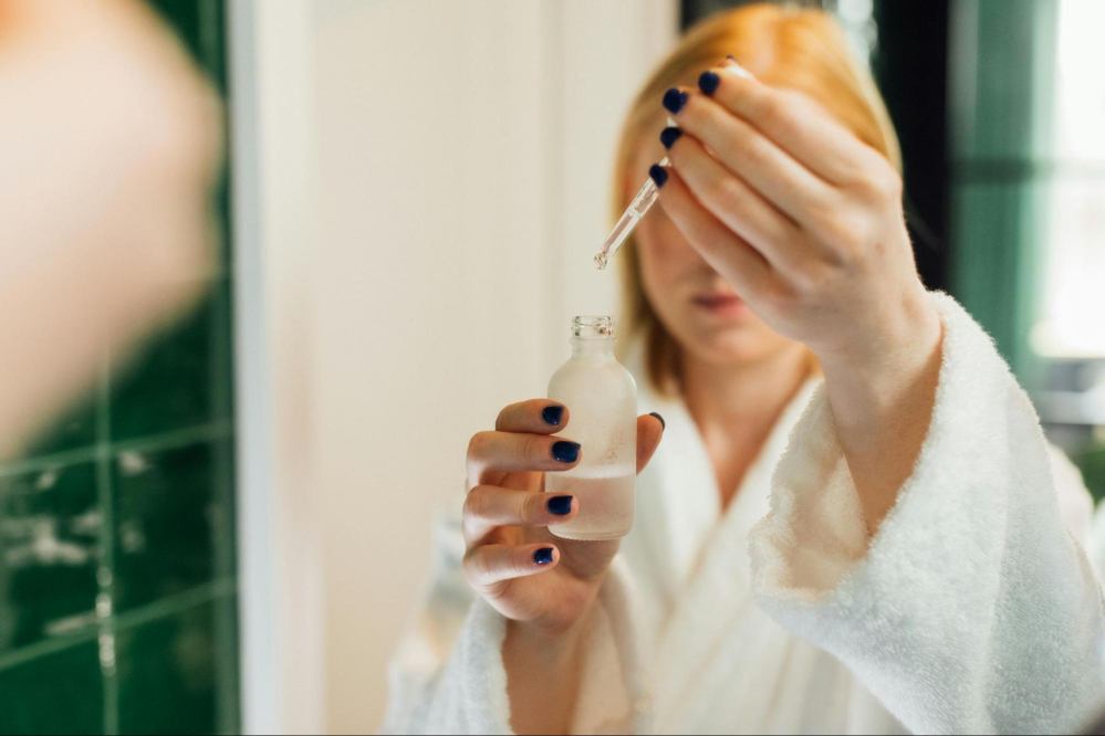 A white woman is taking out the serum from the bottle using a dropper