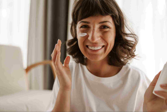 A middle-aged woman is happily applying a vitamin A cream on her ageing skin