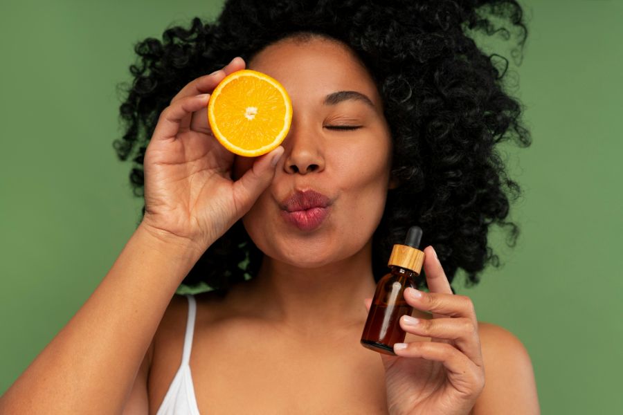 A woman with orange and a vitamin C-infused serum bottle in her hands