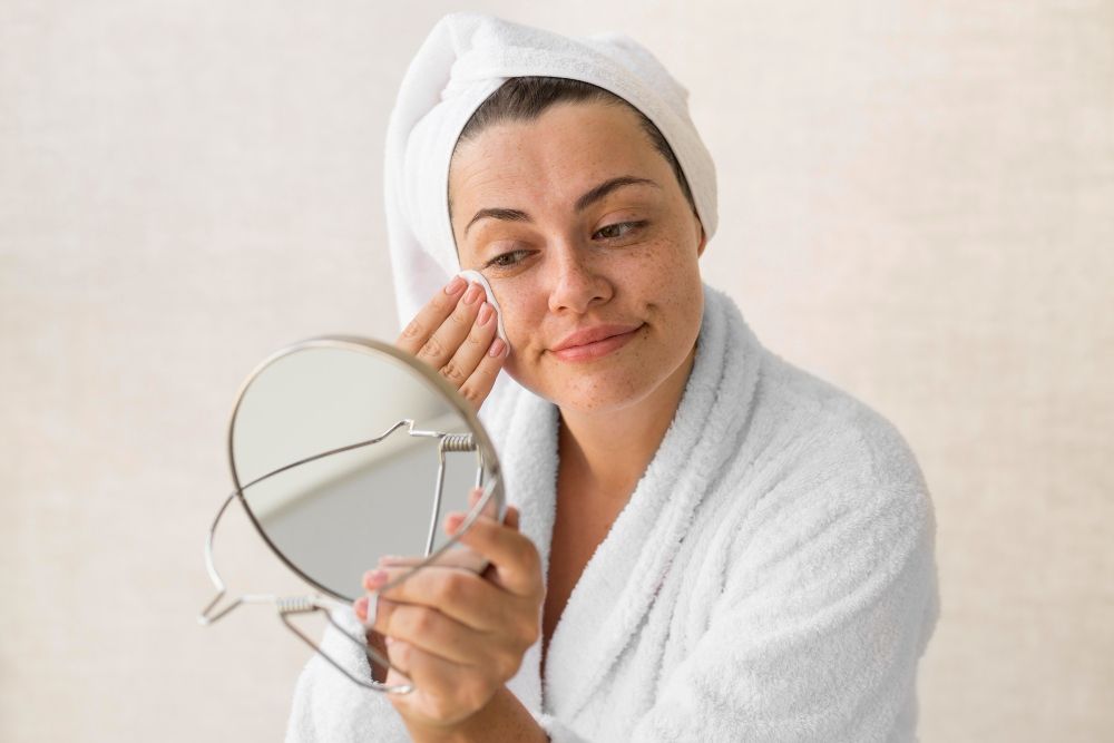 A woman with a compromised skin barrier applying a chemical exfoliant with a cotton pad