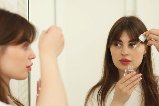 A woman standing in front of the mirror is applying retinoid serum on her face